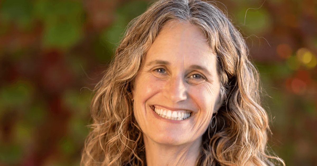 Robin Kaplan smiling outdoors in a navy blouse, with shoulder-length hair and a softly blurred background